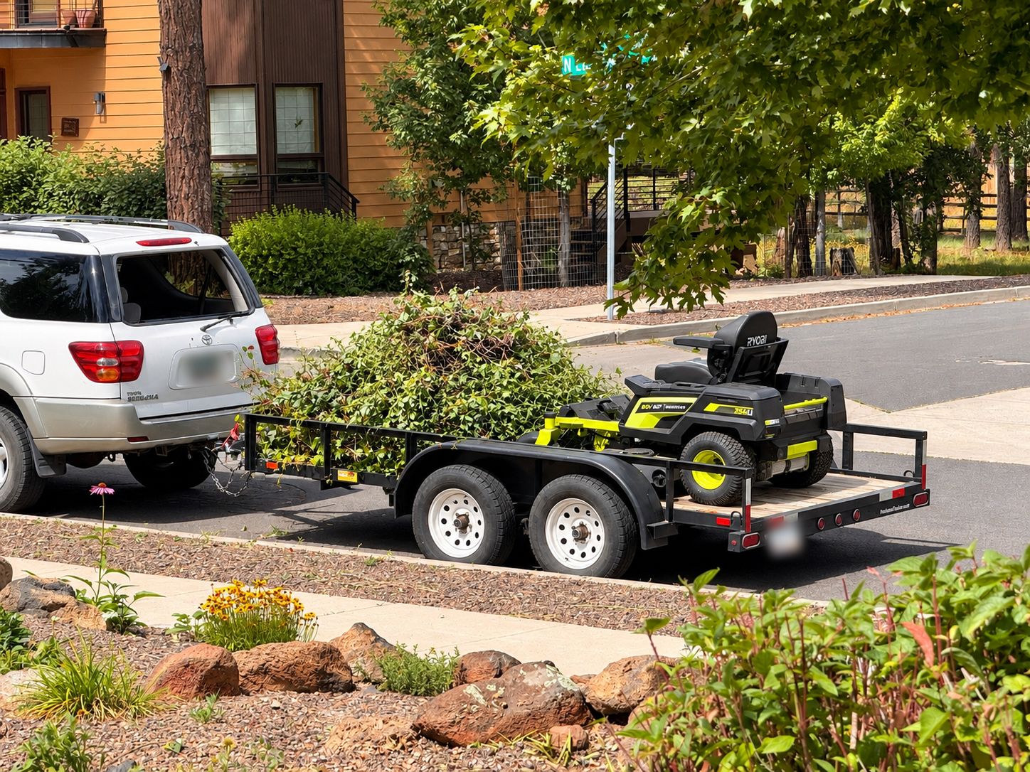 Tandem trailer loaded with cleared brush and a zero turn mower