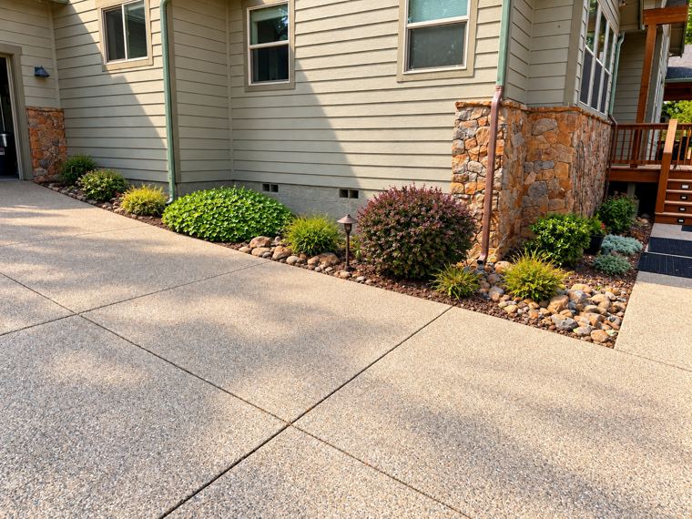 Foundation planting bed with river rock, mulch, shrubs and a path light along a driveway