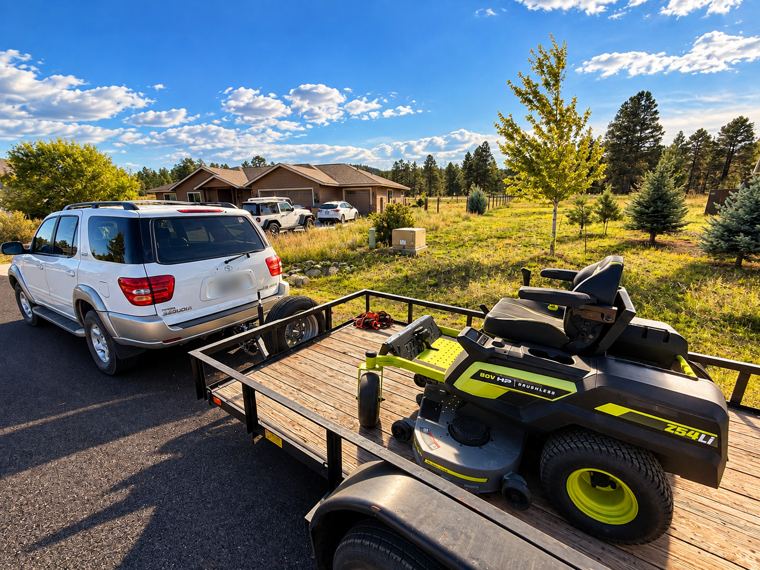 Work trailer with an 80 volt zero turn mower hitched behind a white SUV at a job site